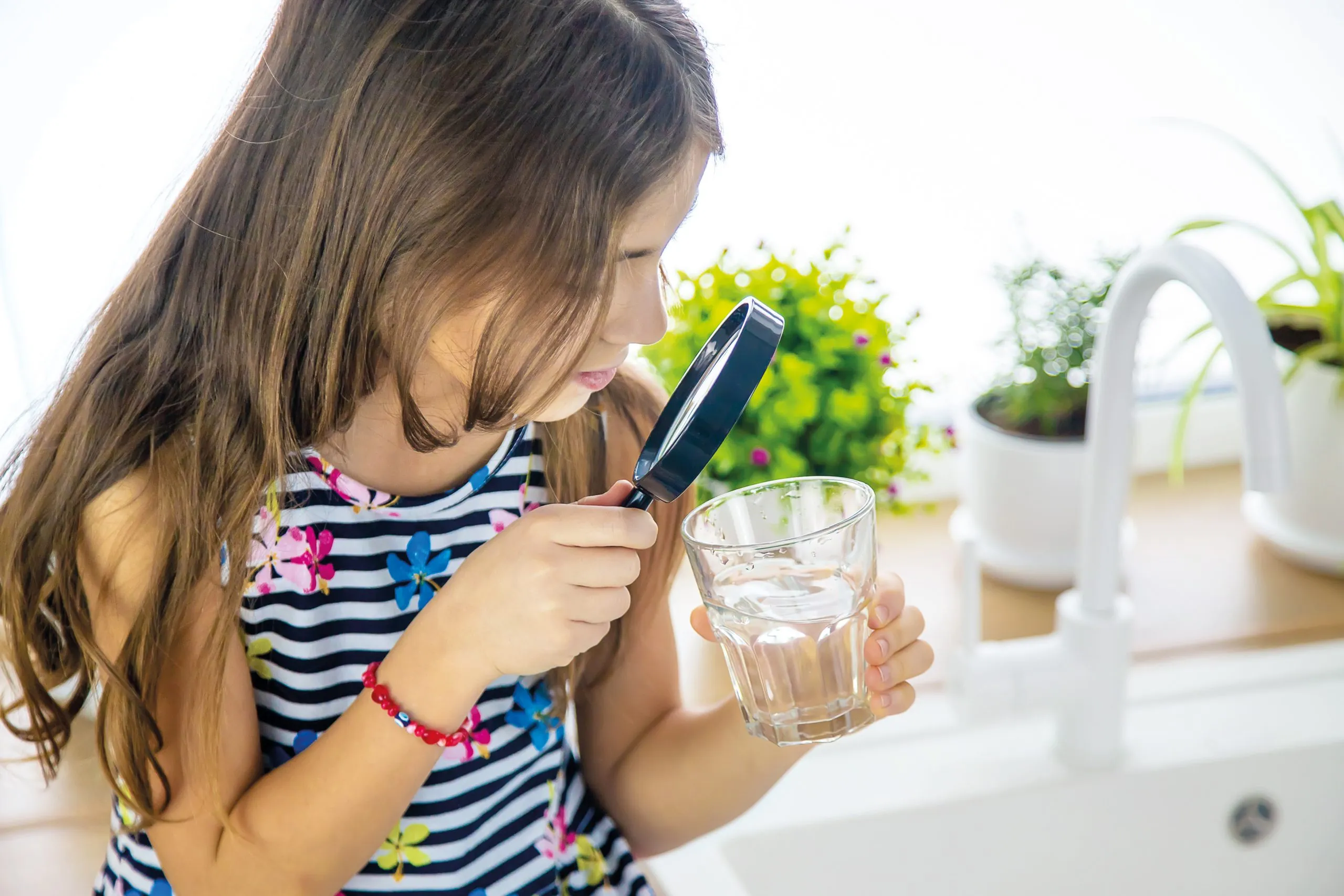 Kind schaut mit Lupe in Wasserglas – Erfahren Sie auf unserem Blog, ob hartes Wasser ungesund ist.